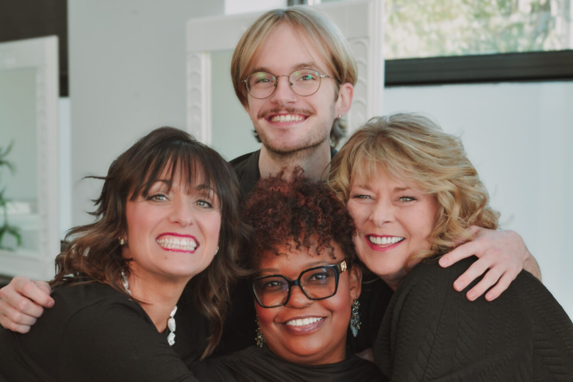 Four friends smiling and posing closely together indoors.