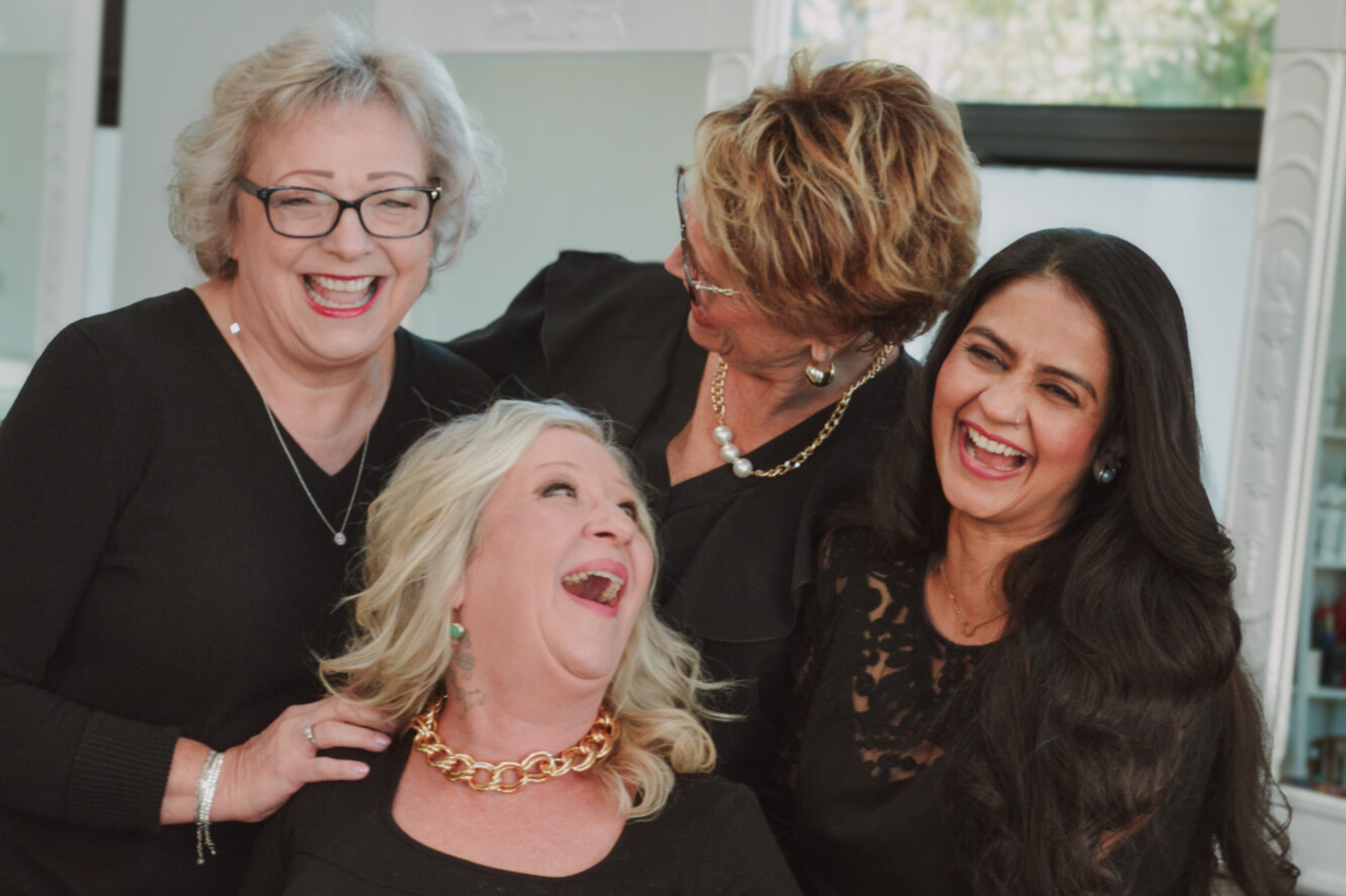 Four women laughing joyfully together in a bright room.